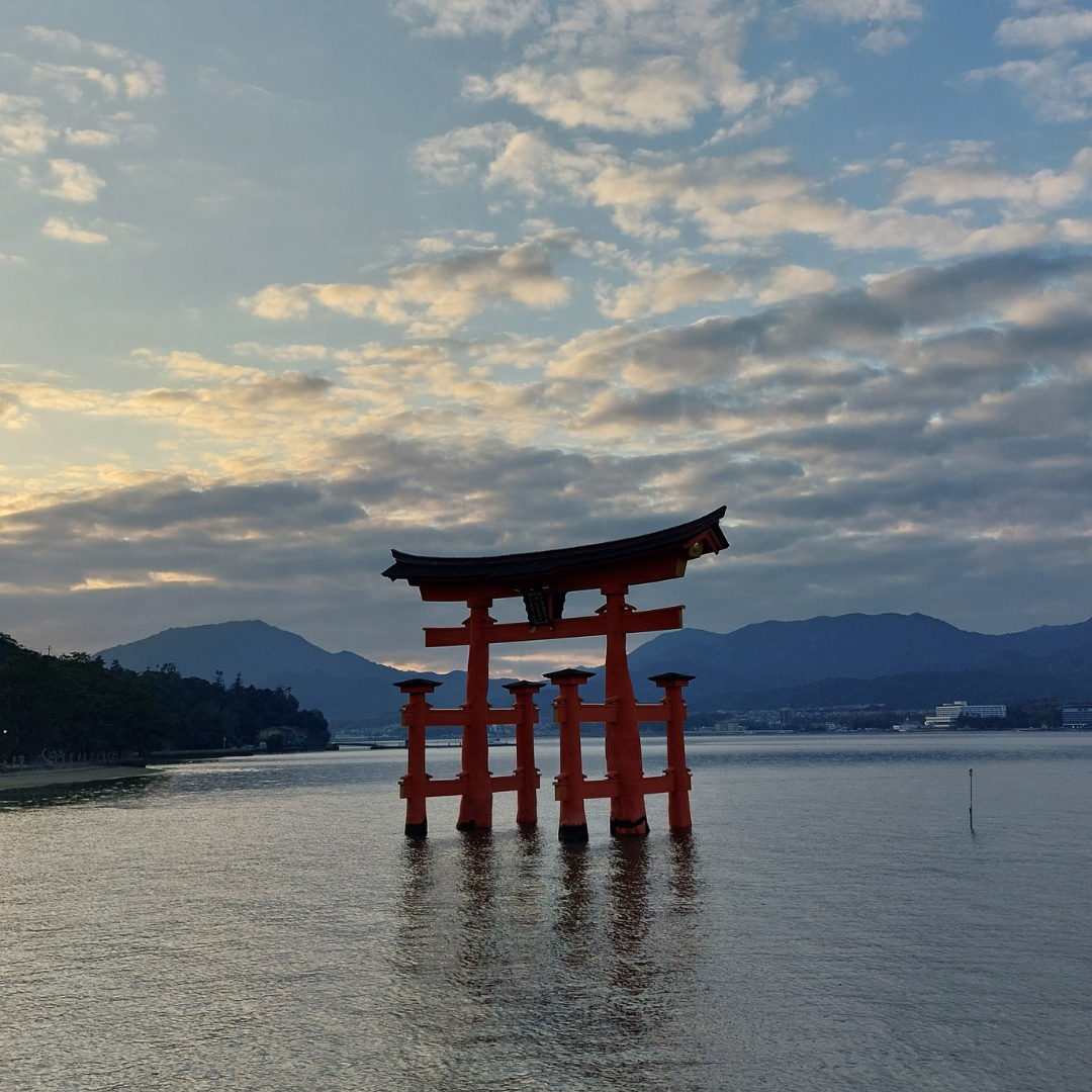 Iconic torii gate of Itsukushima Shrine framed by mountains and sea under the evening sun